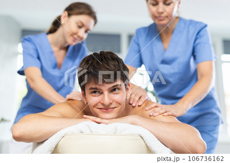 Two female masseurs massaging a man in spa complex Two female masseurs massaging a man in spa complex 106736162