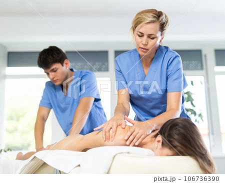 Two female and male masseuses perform stroking and rubbing of muscles of back and shoulders to girl 106736390