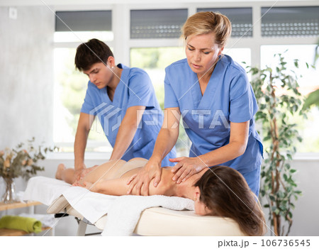 Skilled masseuse performing massage to woman in tandem with assistant 106736545