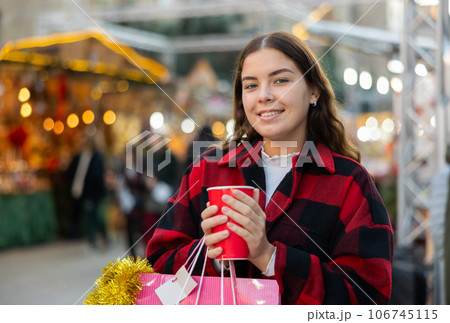 Girl with paper cup of tea walking at street Christmas fair 106745115