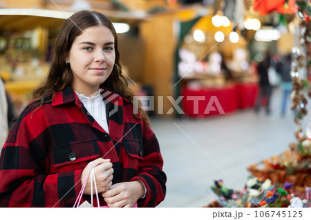 Cheerful girl in plaid coat choosing handmade Christmas decorations at fair 106745125