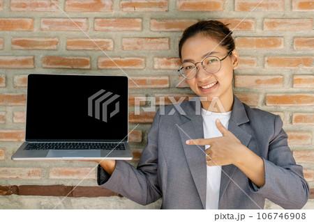 businesswoman holding a laptop and standing in front of red brick background 106746908