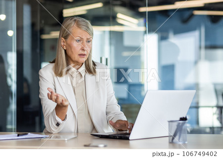 Dissatisfied and disappointed senior gray haired business woman at workplace, female boss received online notification on laptop about poor and unsatisfactory achievement results. Dissatisfied and disappointed senior gray haired business woman at workplace, female boss received online notification on laptop about poor and unsatisfactory achievement results. 106749402