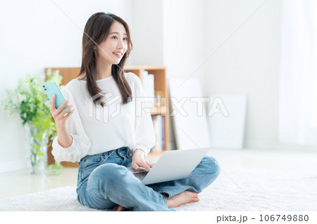 リビングでパソコンとスマホを操作する若い女性 リビングでパソコンとスマホを操作する若い女性 106749880