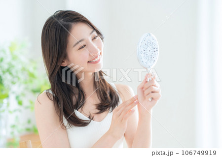 リビングで手鏡を見ながらスキンケアをする若い女性 106749919