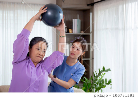 Asian caregiver woman or nurse training senior woman lifting sport ball with hands for exercise. 106751393