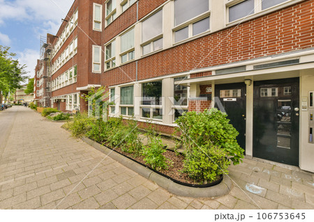 a brick building with plants growing on the sidewalk next to it and an open door that leads to a parking area a brick building with plants growing on the sidewalk next to it and an open door that leads to a parking area 106753645