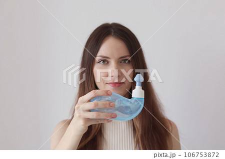 A young woman demonstrates the Neti Pot for treating runny nose and colds. Nasal rinsing, irrigation therapy. A young woman demonstrates the Neti Pot for treating runny nose and colds. Nasal rinsing, irrigation therapy. 106753872