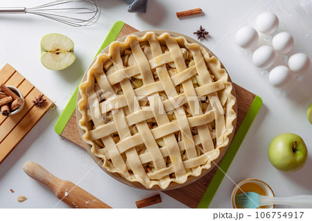 Uncooked apple pie into a baking dish ready for cooking on a white table surrounded by ingredients Uncooked apple pie into a baking dish ready for cooking on a white table surrounded by ingredients 106754917