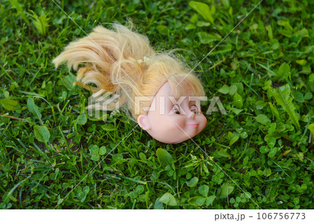 A doll's head with spoiled blond hair, discarded in a park meadow. A doll's head with spoiled blond hair, discarded in a park meadow. 106756773