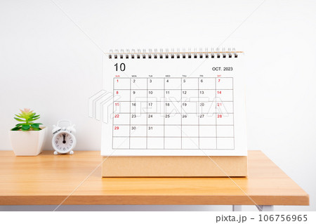 The October Monthly desk calendar for 2023 year and alarm clock on wooden table. 106756965