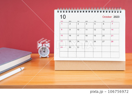 The October Monthly desk calendar for 2023 year and alarm clock on wooden table. 106756972