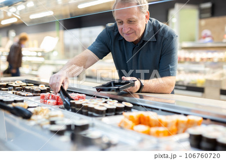 Mature customer selects Japanese rolls with interest in the grocery department of supermarket Mature customer selects Japanese rolls with interest in the grocery department of supermarket 106760720