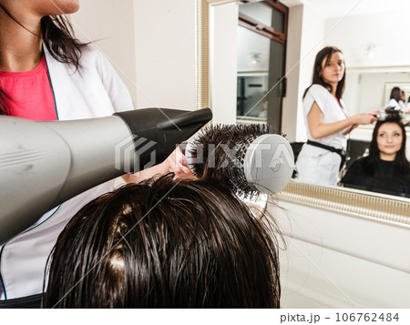 Hairdresser drying dark female hair using professional hairdryer Hairdresser drying dark female hair using professional hairdryer 106762484