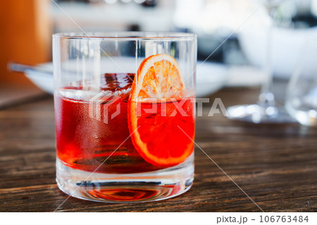 Negroni cocktail in old fashion glass with orange slice on wooden table. Negroni cocktail in old fashion glass with orange slice on wooden table. 106763484