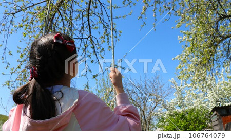 a girl from the back with brown hair and plaid bows in a pink jacket swings on a homemade rope swing in a spring garden or park with flowering trees, positive children's emotions when walking a girl from the back with brown hair and plaid bows in a pink jacket swings on a homemade rope swing in a spring garden or park with flowering trees, positive children's emotions when walking 106764079