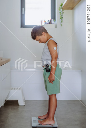 A young boy with diabetes weighing himself on bathroom scale A young boy with diabetes weighing himself on bathroom scale 106764292