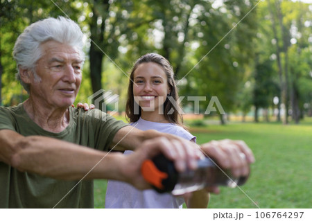The senior man exercising in the park, using a water bottle as a dumbbell. The senior man exercising in the park, using a water bottle as a dumbbell. 106764297