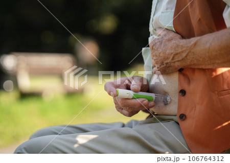 Diabetic senior patient injecting insulin in belly outdoors. 106764312
