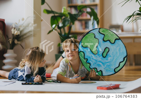 Siblings lying on stomach and painting at home with watercolors, markers and tempera paints, creating a model of planet Earth. Siblings lying on stomach and painting at home with watercolors, markers and tempera paints, creating a model of planet Earth. 106764383