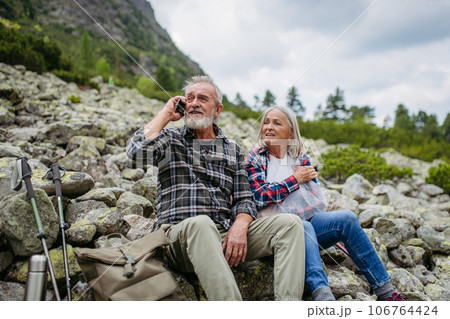 Senior tourists sitting on rocks and looking at the distant nature through binoculars. 106764424