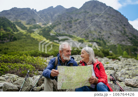 Senior tourists sitting on rocks and looking at the route on a map. 106764426