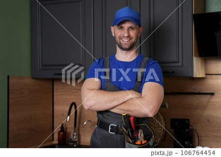 Smiling handsome plumber standing with crossed arms and looking at camera in kitchen 106764454