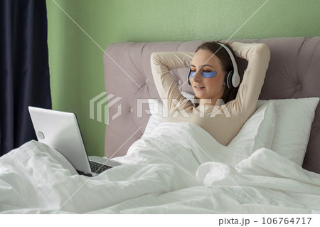 Woman lying in bed listening to music, audiobook, podcast, enjoying meditation for sleep and peace of mind in wireless headphones. Woman lying in bed listening to music, audiobook, podcast, enjoying meditation for sleep and peace of mind in wireless headphones. 106764717