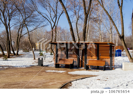 Wooden bench in the spring park. Bright spring sun and snow in the park. Place to rest for a walk. Morning walk. Wooden bench in the spring park. Bright spring sun and snow in the park. Place to rest for a walk. Morning walk. 106765654