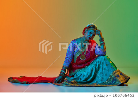 Indian culture. Mature, beautiful indian woman in traditional clothes, dress posing against gradient studio background in neon light 106766452