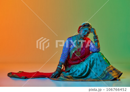 Indian culture. Mature, beautiful indian woman in traditional clothes, dress posing against gradient studio background in neon light Indian culture. Mature, beautiful indian woman in traditional clothes, dress posing against gradient studio background in neon light 106766452