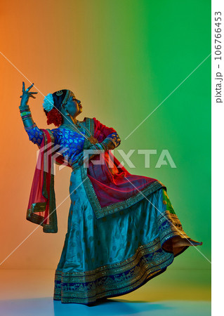 Indian culture. Mature, beautiful indian woman in traditional clothes, dress posing against gradient studio background in neon light Indian culture. Mature, beautiful indian woman in traditional clothes, dress posing against gradient studio background in neon light 106766453