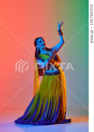 Odissi dance. Beautiful woman in indian costume, with makeup and accessories dancing against gradient studio background in neon light 106766459