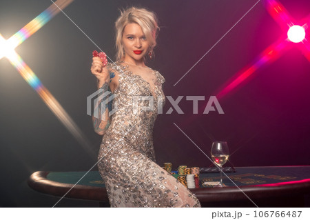 Blonde woman with a beautiful hairstyle and perfect make-up is posing with red gambling chips in her hands. Casino, poker. 106766487
