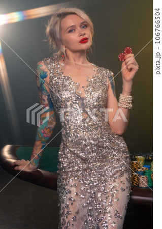 Blonde woman with a beautiful hairstyle and perfect make-up is posing with red gambling chips in her hands. Casino, poker. Blonde woman with a beautiful hairstyle and perfect make-up is posing with red gambling chips in her hands. Casino, poker. 106766504