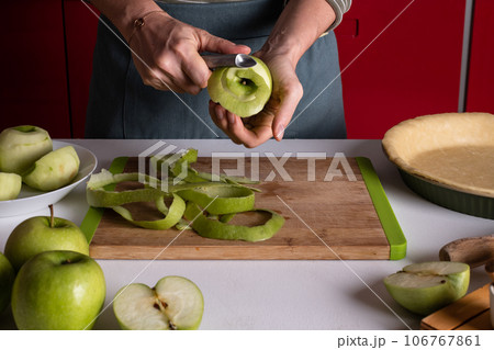 Woman is peeling apples to prepare apple pie in the kitchen. Authentic female hands peel an apple 106767861