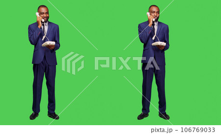 Confident employee answering landline phone call, having remote conversation on office telephone line with cord in studio. Male manager talking on phone, full body green screen. Confident employee answering landline phone call, having remote conversation on office telephone line with cord in studio. Male manager talking on phone, full body green screen. 106769033