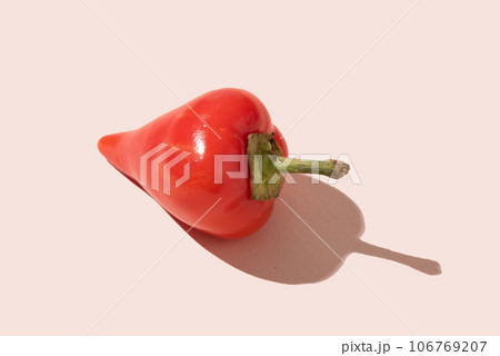 A pod of red hot pepper with a hard shadow on a light pink background. 106769207