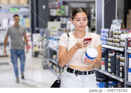Interested young woman scanning barcode on paint can in construction hypermarket 106770782