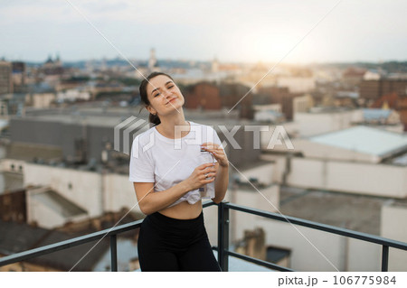 Yogini with water bottle watching sunset on building roof 106775984