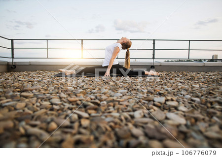 Adult practicing front split while gazing at sky on rooftop Adult practicing front split while gazing at sky on rooftop 106776079