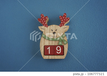 Festive wooden deer with Viva Magenta cubes 19 on blue background close-up top view. Christmas concept of date or time 106777321