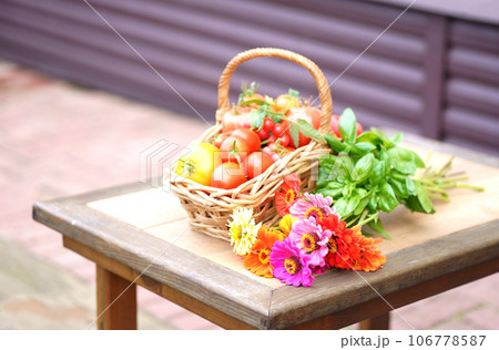 Red and yellow tomatoes in a basket next to a bunch of flowers 106778587