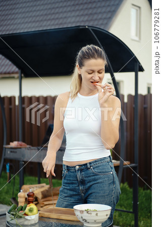 A woman rests her knife on a board and bites a cucumber 106779281