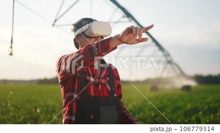 agriculture virtual reality. a farmer in virtual reality glasses controls a machine to irrigate corn field. agriculture virtual reality concept. business a farmer vr in works in field with corn 106779314