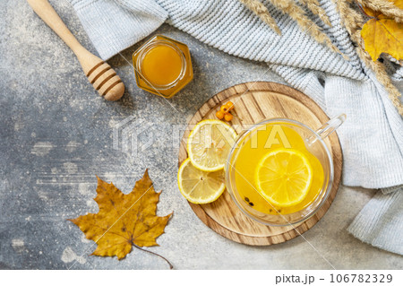 Hot herbal vitamin sea buckthorn tea in a glass cup with fresh sea buckthorn berries, honey and lemon on a stone tabletop. Relaxation and herbal medicine. View from above. Copy space. Hot herbal vitamin sea buckthorn tea in a glass cup with fresh sea buckthorn berries, honey and lemon on a stone tabletop. Relaxation and herbal medicine. View from above. Copy space. 106782329