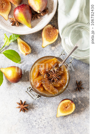 Homemade fig sweet jam in a glass jar with fresh figs on a light gray table. Autumn harvest preservation, healthy fermented food. View from above. 106782430
