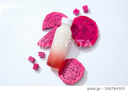 Top view of red dragon fruit decorated with a bottle without label. White background. Dragon fruit (Hylocereus) is an exotic fruit that is high in fiber 106784303