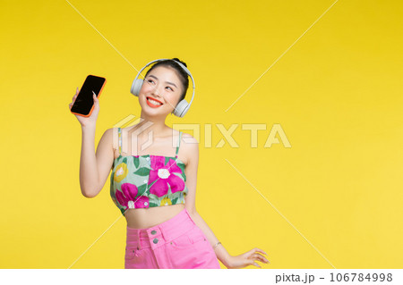 Young Asian woman wearing headphones dancing and listening to music from smartphone 106784998