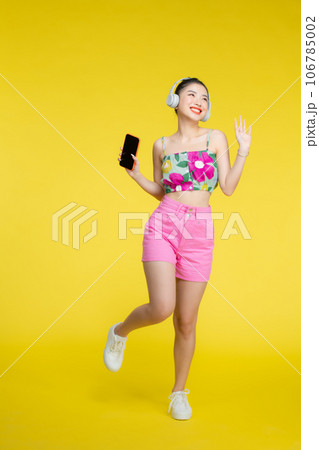 woman wearing headphones listening to music from smartphone on colorful yellow isolated background 106785002